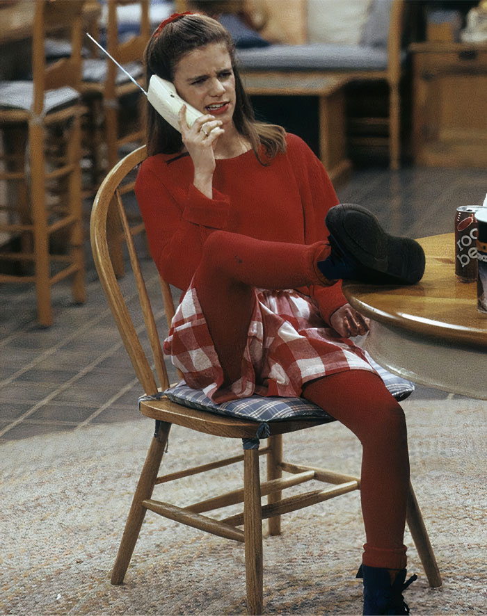 Kimmy Gibbler speaking by phone with one leg lying on the table