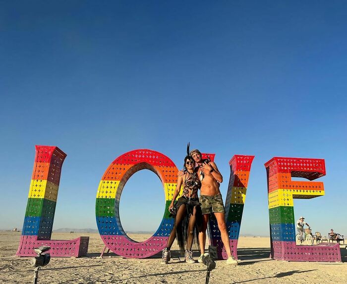 Colourful love sign in the desert and two people in front of it 