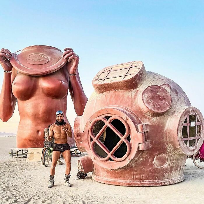 Man taking photo near an ancient diving helmet installation and woman's torso figure 