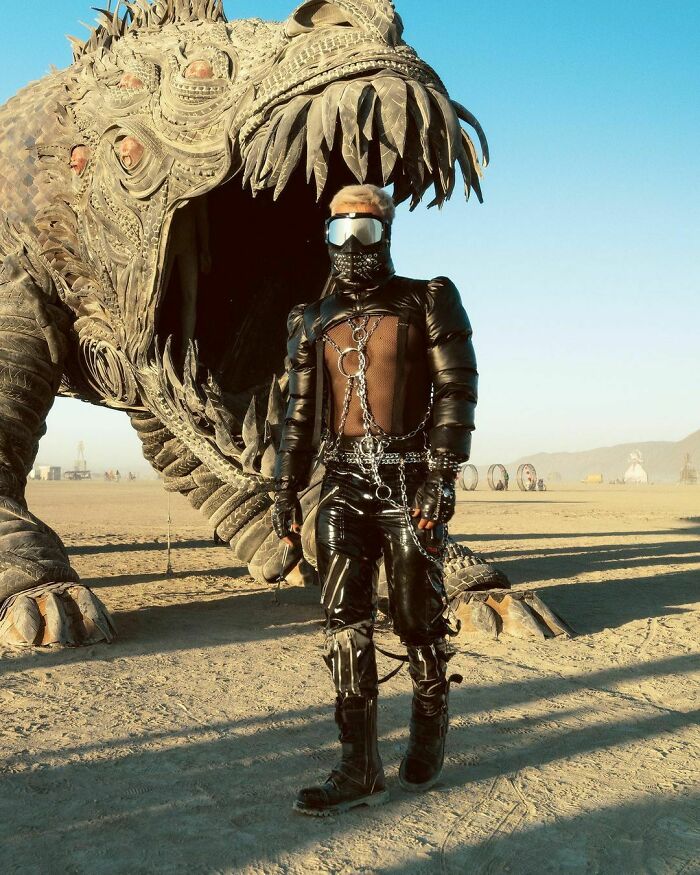 Male wearing leather suite and goggles with statue of a dragon behind him