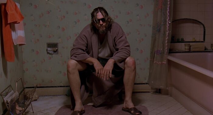 The dude is sitting on the toilet 