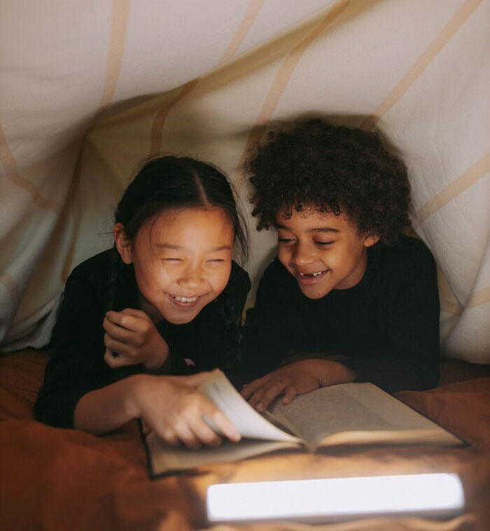 Brother And Sister Reading Book Under Blanket 