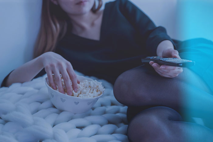 a woman sitting with a remote controller near the bowl of popcorn