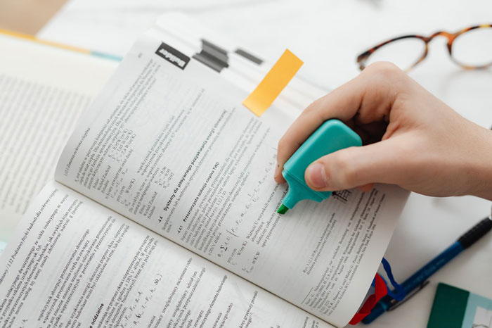 a person marking something in the book with a help of highlighter