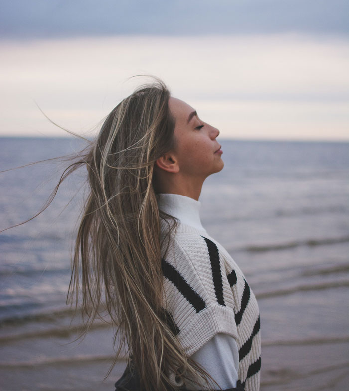 a woman with closed eyes standing near the sea