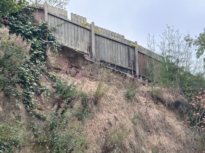 This Hillside Fence Is Completely Undermined. If No Action Is Taken To Fix The Issue The Hillside Will Continue To Erode Causing The Fence To Fail Entirely