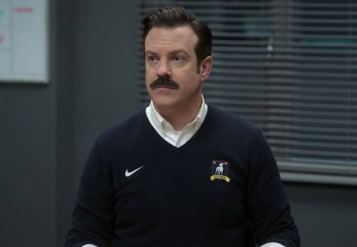 Ted Lasso wearing blue sweater and white shirt