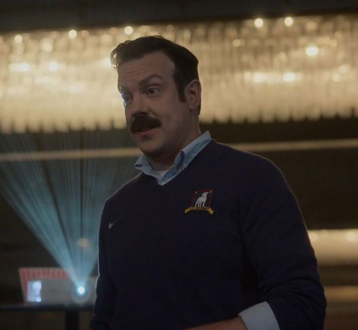 Ted Lasso wearing blue sweater and white shirt