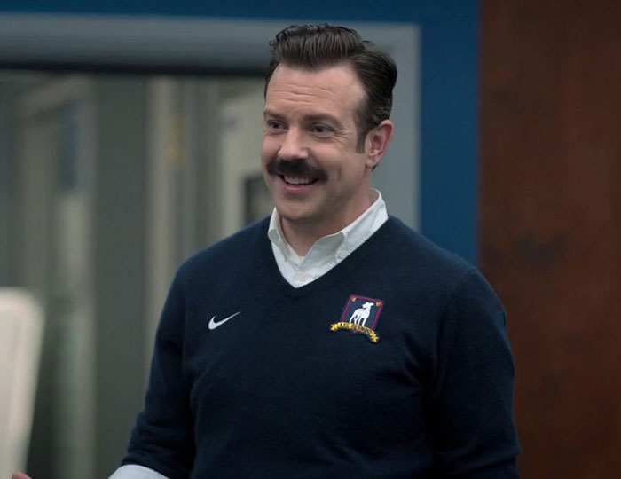 Ted Lasso wearing blue sweater and white shirt