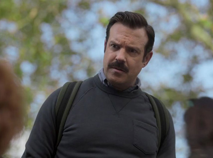 Ted Lasso wearing gray sweater and white shirt