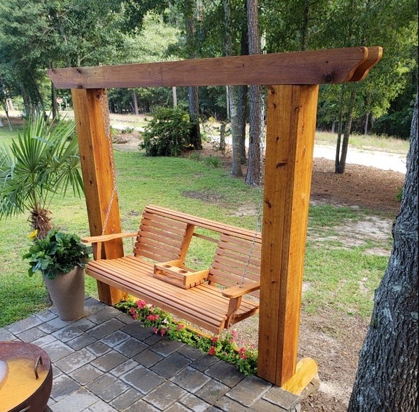 A chain-based wooden console porch swing surrounded by plants and flowers