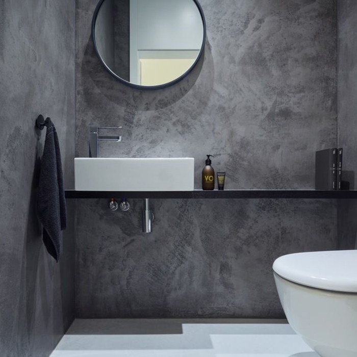 Gray textured concrete wall with round mirror in bathroom