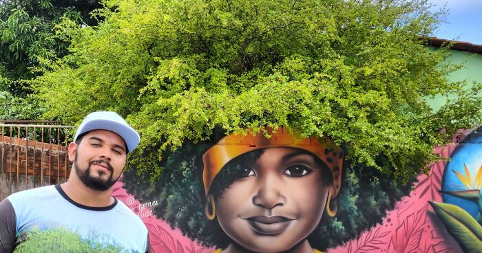 Street Artist Continues To Paint Portraits On Walls Next To Trees That Double As Hair