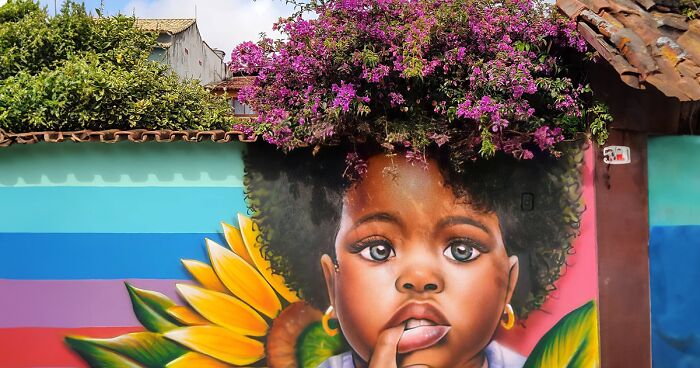 Street Artist Continues To Paint Portraits On Walls Next To Trees That Double As Hair