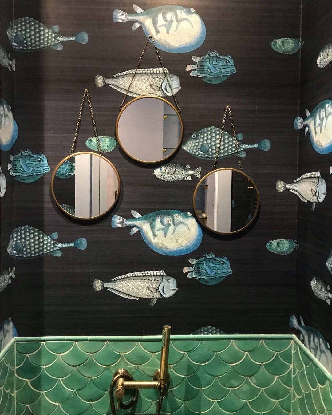 Bathroom with three mirrors, a water-themed sink, and wallpaper with fish designs