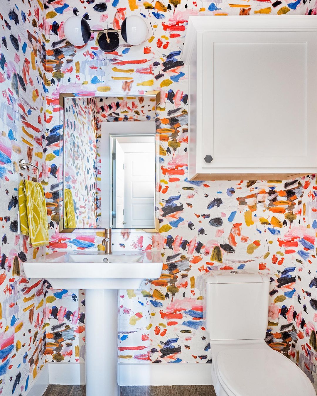 Bathroom with colorful paint swatch wallpaper with white sink and toilet