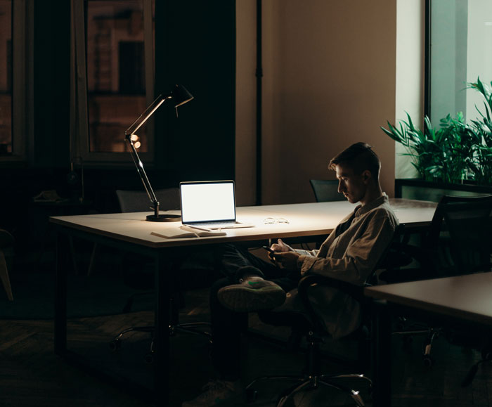 a man sitting in the darkness on chair in front of macbook