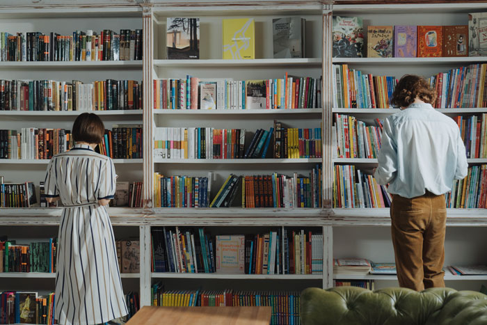 a man in a white dress shirt standing beside a brown wooden bookshelf