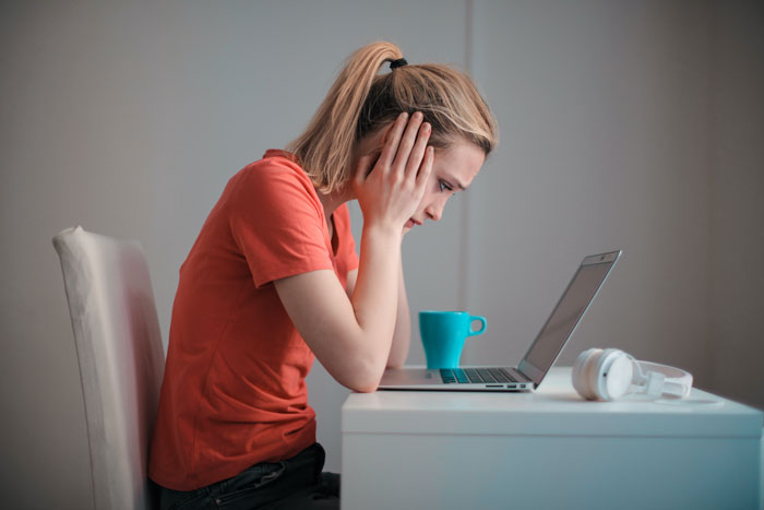 a woman sitting near the laptop with hands holding her head