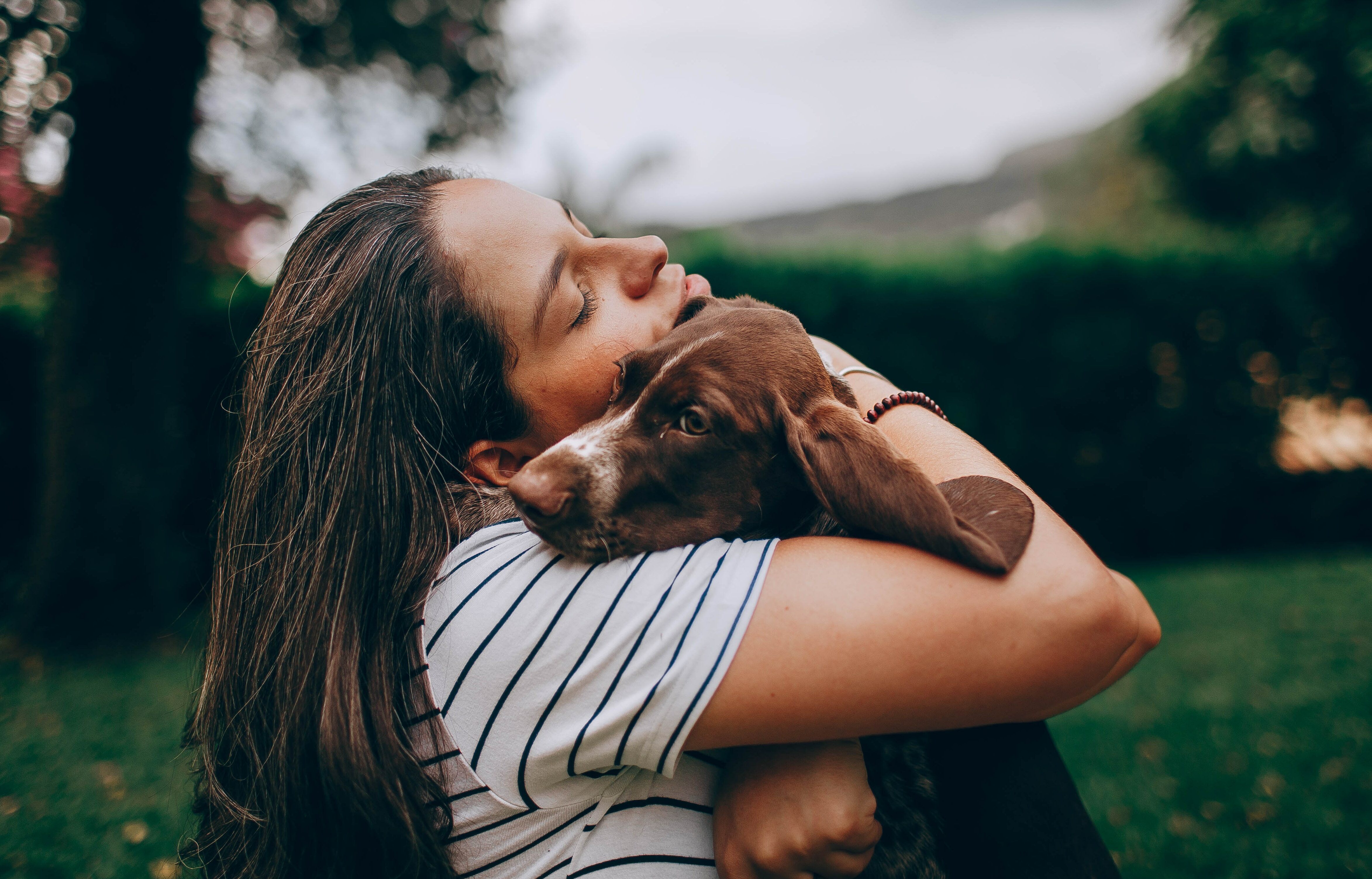 woman in white and black stripe shirt hugging brown short coated dog