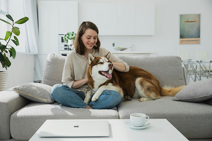 A Young Woman Sitting on a Couch Petting her Dog 