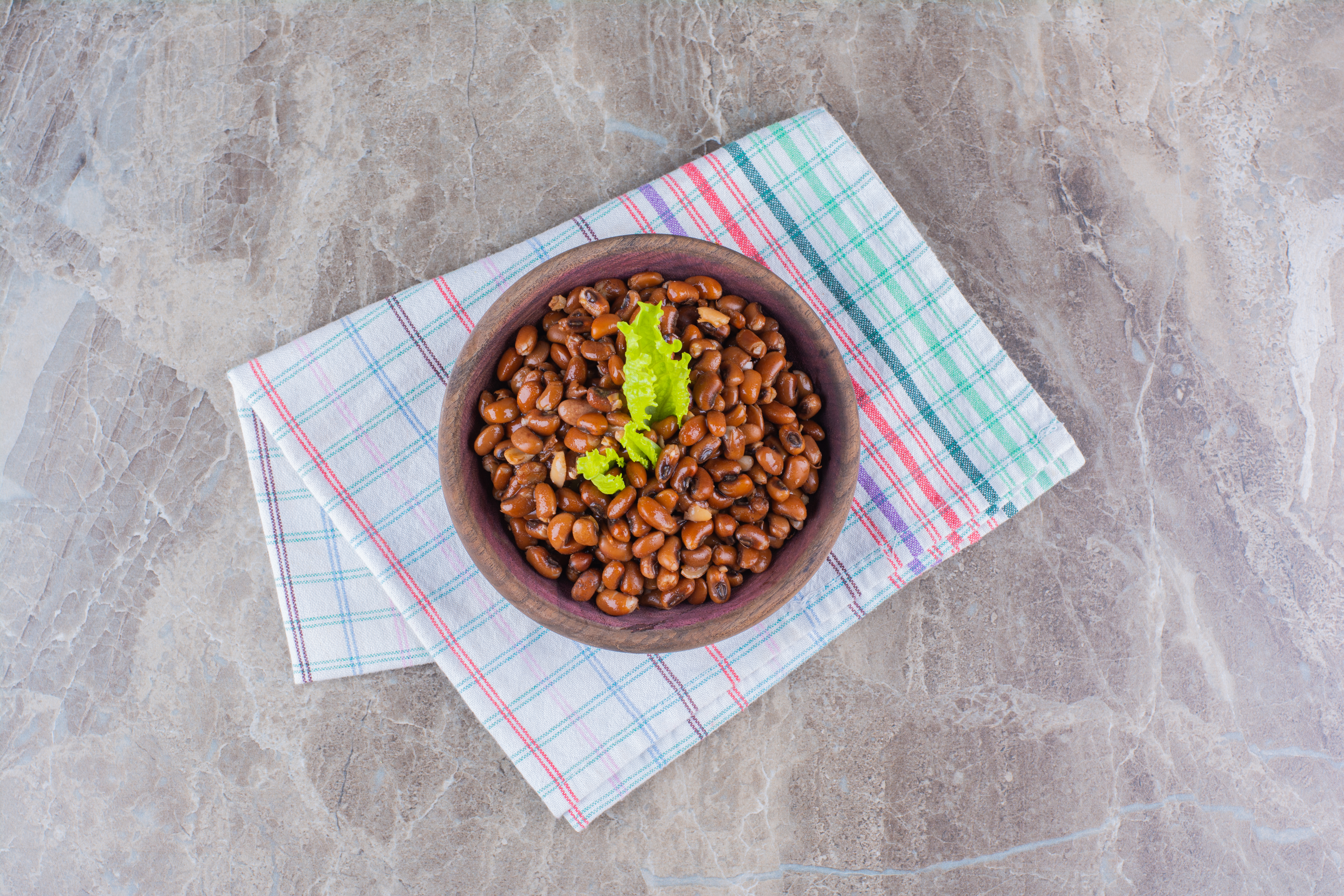 Wooden bowl of boiled beans with tablecloth on marble surface