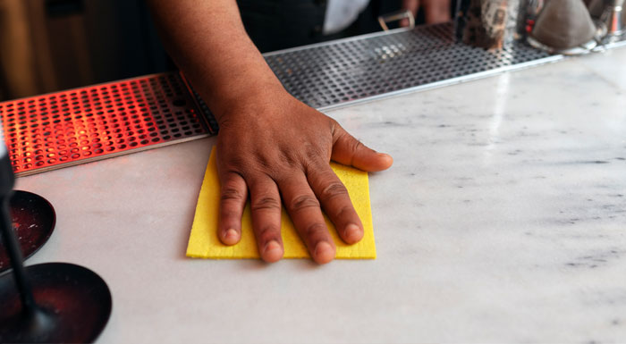 A person wearing gloves and cleaning a white granite countertop