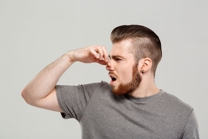 man covers nose with hand showing that something stinks