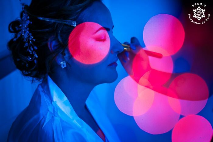 Bride in artistic blue and pink lighting, applying makeup; selected by Premios FdB for incredible wedding photos 2024.