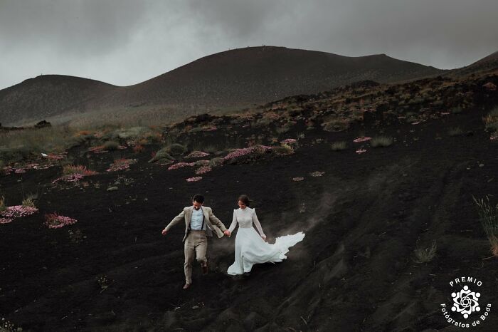 Bride and groom running down a volcanic landscape, capturing an incredible wedding photo by Premios FdB.