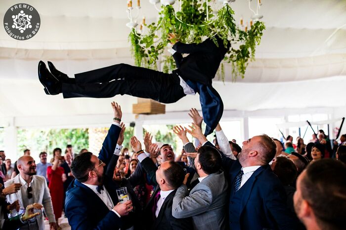 Group of people joyfully tossing a groom into the air at a wedding celebration, capturing an incredible wedding photo moment.