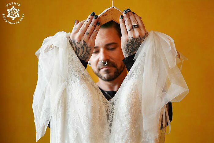 Tattooed person holding a lace wedding dress on a hanger, showcasing one of the incredible wedding photos of 2024.