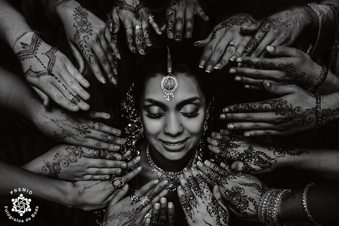 Bride with intricate henna designs surrounded by hands in a stunning wedding photo selected by Premios FdB.