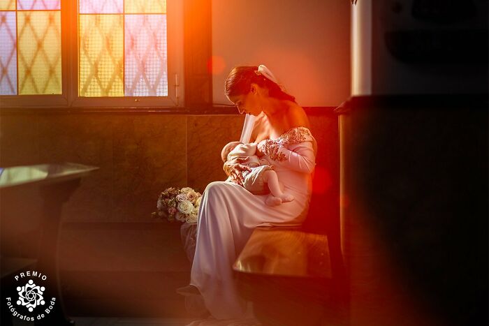 Bride in a white dress, holding a baby in a warmly lit room, showcasing incredible wedding photography.