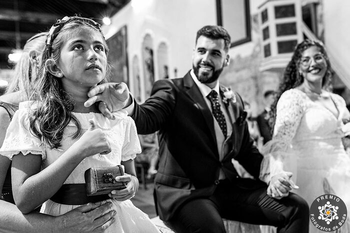 A touching wedding moment with a smiling groom in a suit and a thoughtful girl holding a camera, captured by Premios FdB.