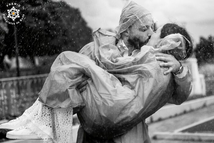 A couple kissing passionately in the rain, wearing raincoats, capturing an incredible wedding moment.