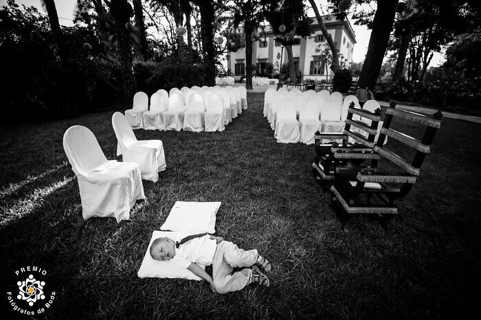 Child napping on grass at an outdoor wedding, surrounded by white covered chairs, captured by Premios FdB.