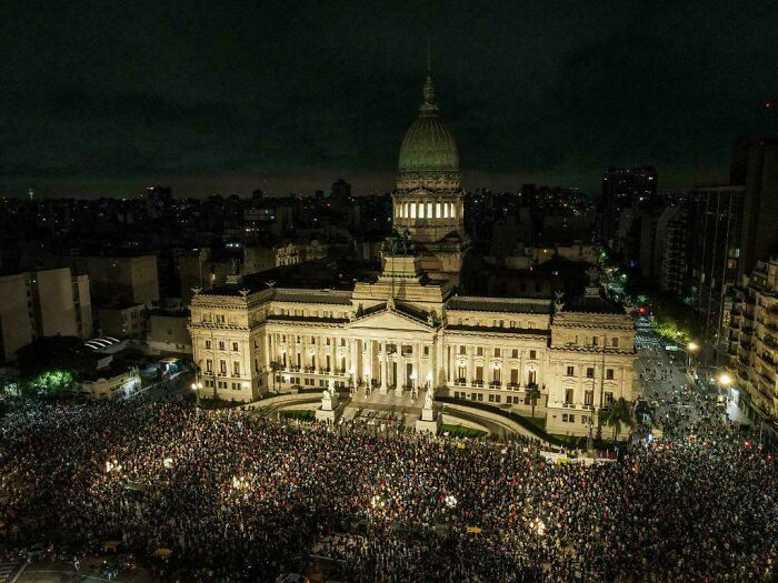 Crowds gathered at a grand building at night, suggesting a boring dystopia atmosphere.