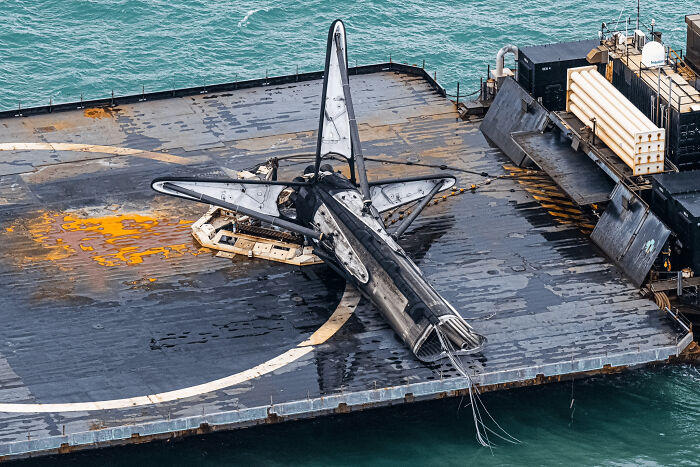 A damaged spacecraft on a landing pad by the ocean, illustrating an expensive unfortunate incident.