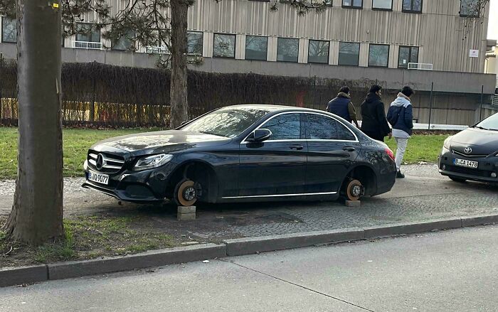 Luxury car missing wheels on a sidewalk, likely an unfortunate incident costing a fortune.