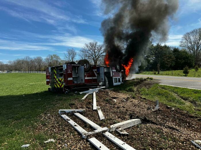 Overturned fire truck on fire at roadside, with smoke billowing, possibly an unfortunate incident indicating high costs.