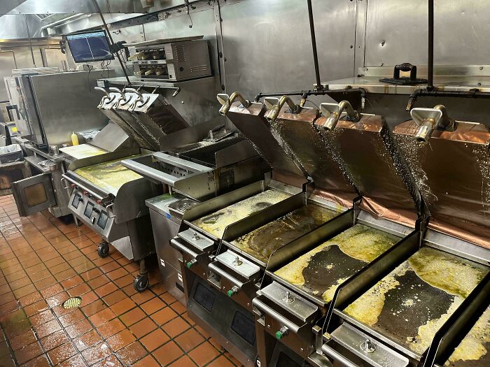 Industrial kitchen with overflowing oil from fryers, suggesting a costly cleanup.