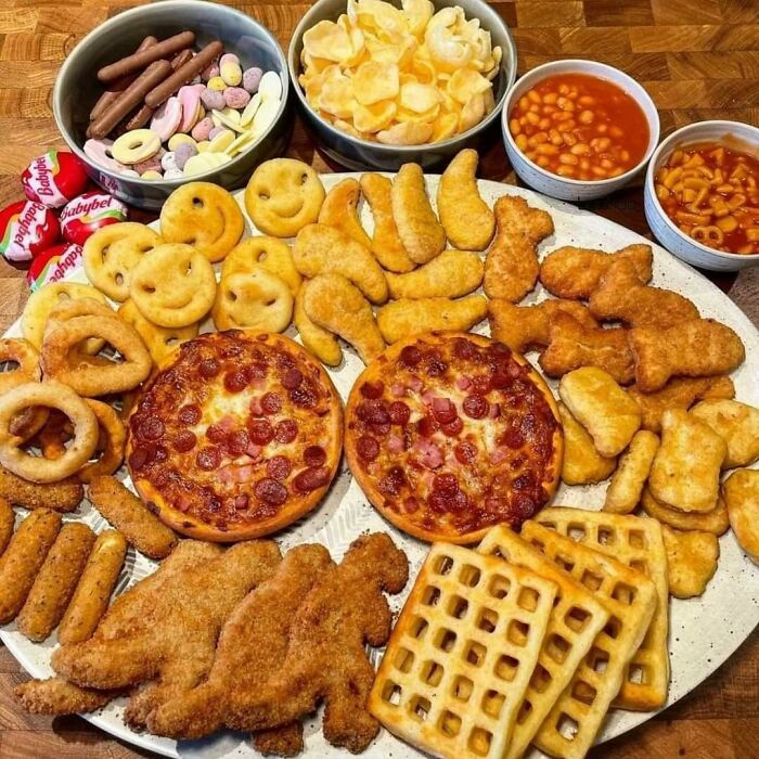 A variety of classic British snacks including mini pizzas, chicken nuggets, crisps, beans, and waffles on a platter.