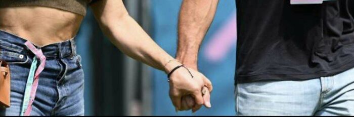 Two people holding hands, contrasting skin tones and wristbands, against a blurred background.