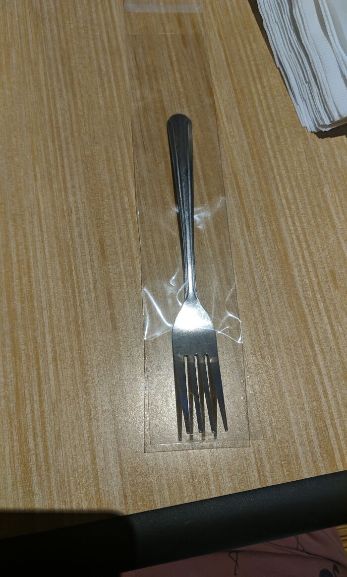 Fork packaged incorrectly in plastic wrap, showcasing wrong product packaging on a wooden table.