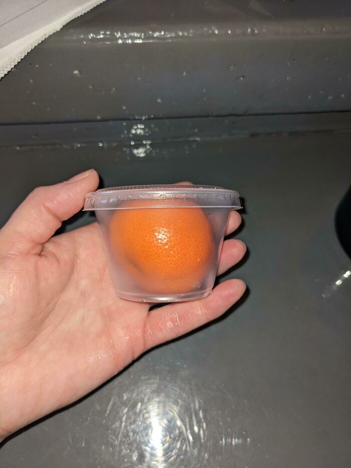 Hand holding an orange packaged in a plastic cup, showcasing wrong product packaging design.