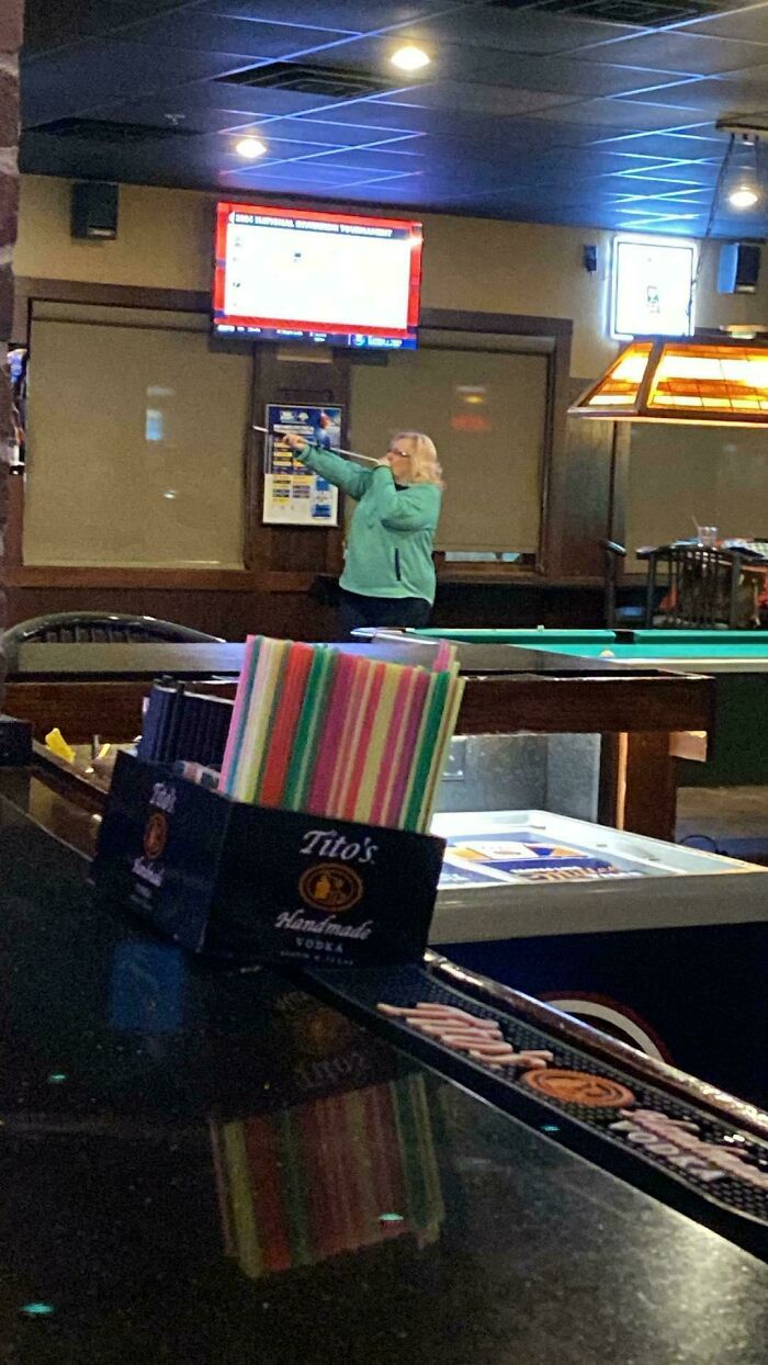 Señora en un bar jugando a los dardos... con una cerbatana