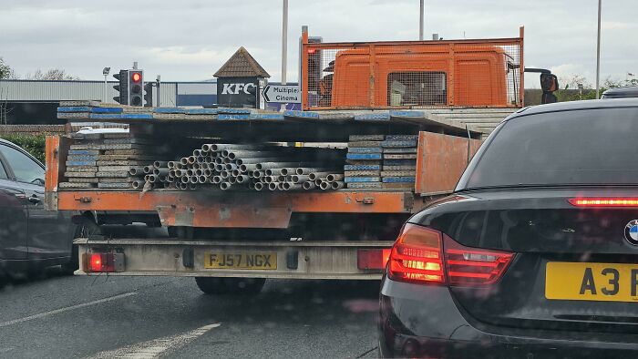 Truck loaded with metal pipes in UK traffic near a KFC sign, showcasing British road scenes.