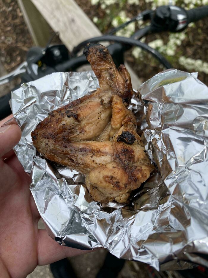 Grilled chicken wing wrapped in foil held by a hand, showcasing a delightfully British takeaway moment.