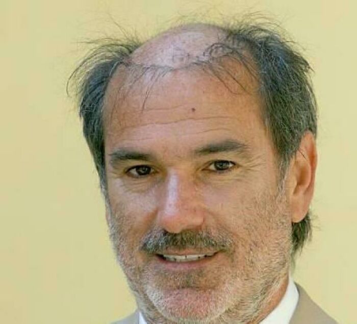 Man with thinning hair and a beard, smiling slightly against a yellow background.